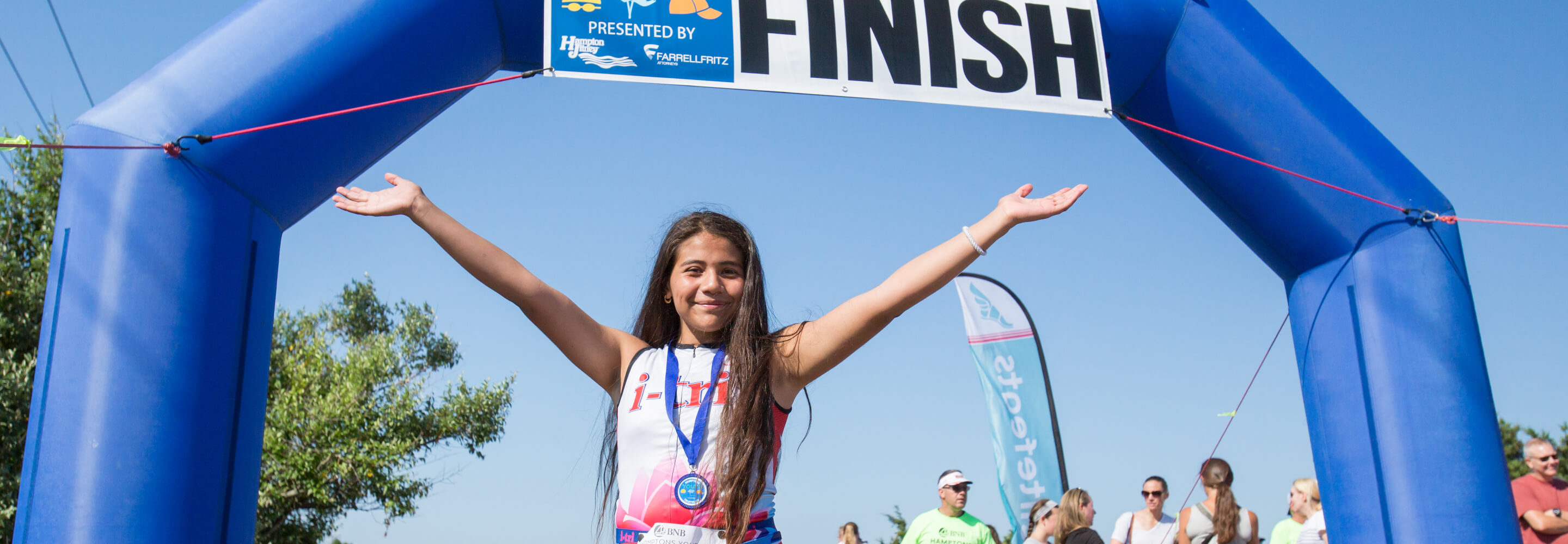 A girl wearing a medal holds her arms up in triumph at the race finish line