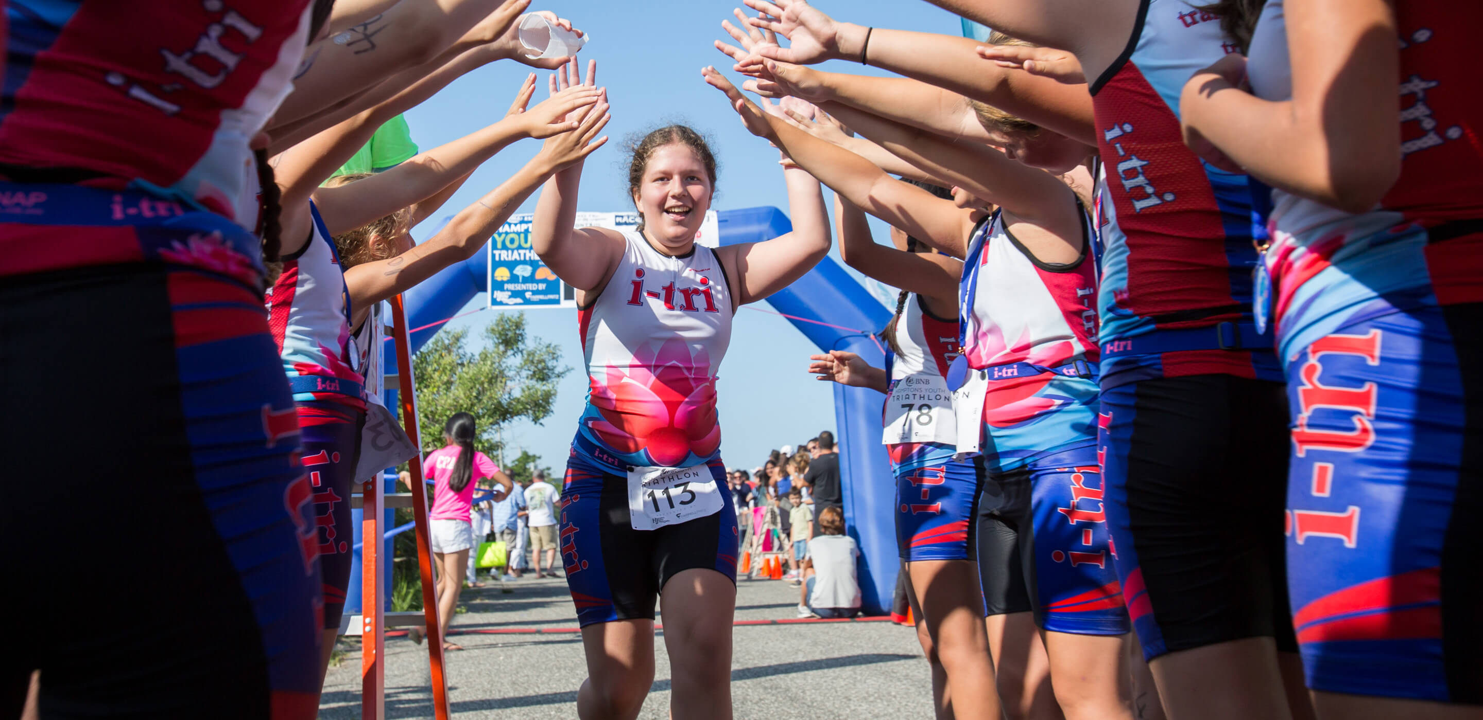Girl in i-tri race uniform runs through a line of others giving high-fives