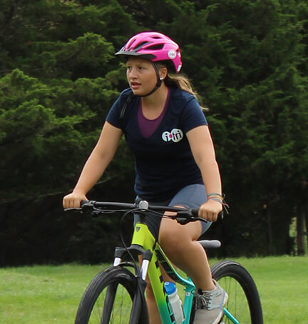 A girl in i-tri branded helmet and shirt rides her bicycle